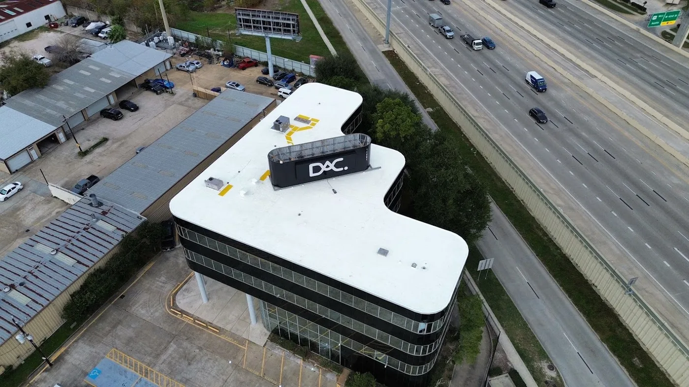 Aerial view of a completed white membrane roof on a curved office building beside a Houston freeway