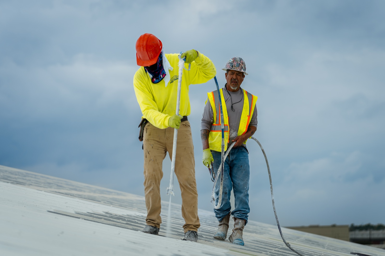 Crew spraying white elastomeric coating across a metal roof