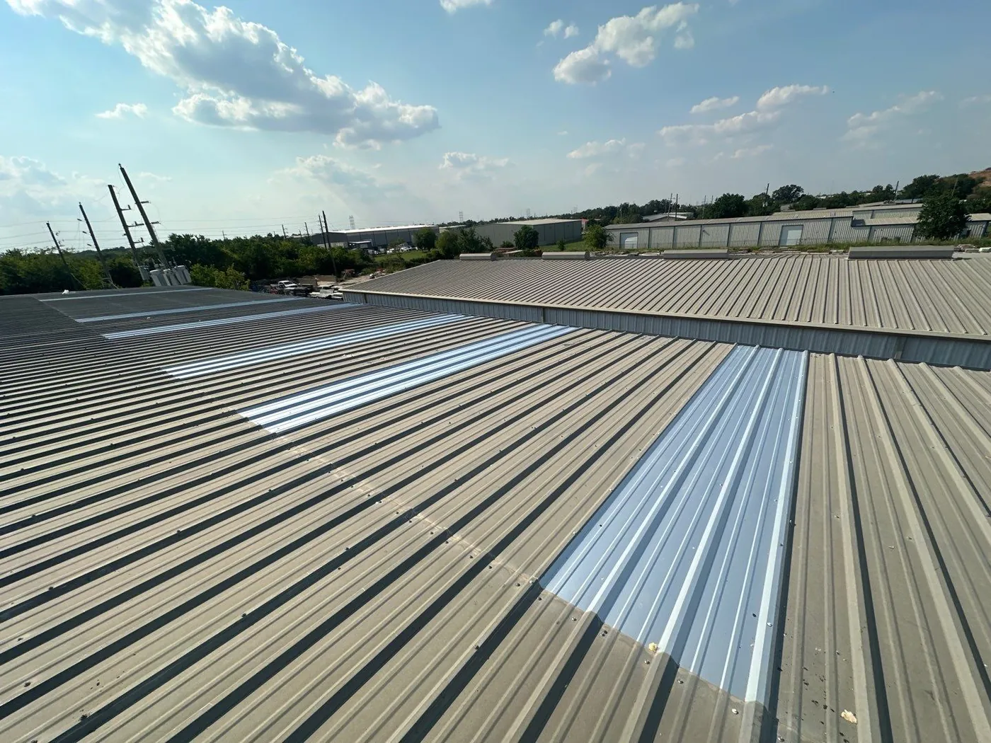 An aged tan ribbed metal roof with several new, bright panel sections set into the field