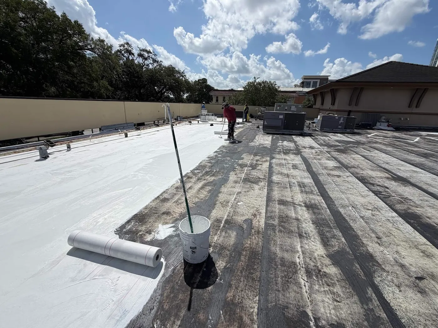 A commercial roof part way through a restoration, a darker banded layer over one half and the white top coat over the other, with rooftop units and a parapet wall beyond